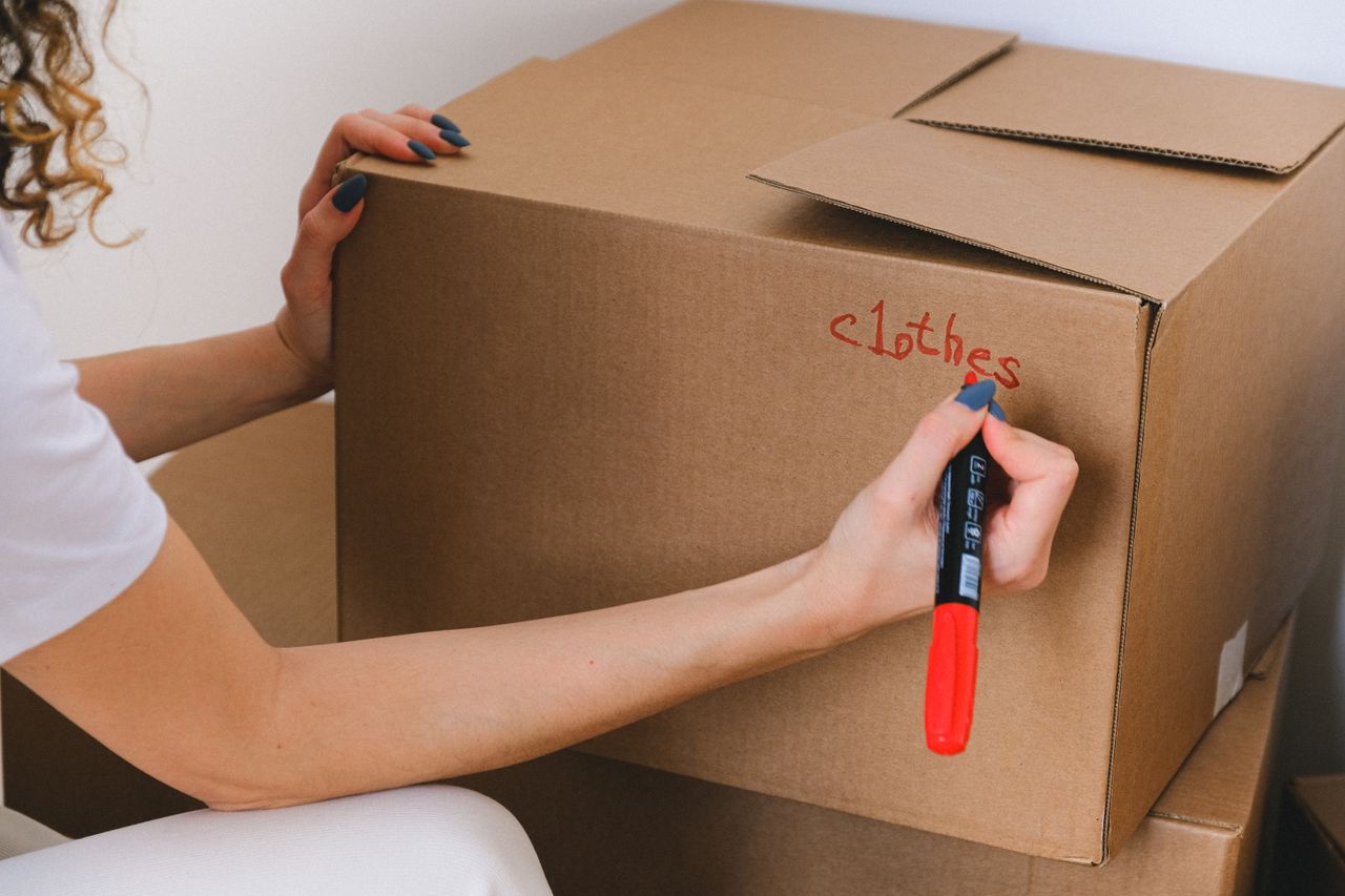 services-07 Close-up of a woman labeling a cardboard box with a red marker indoors.
